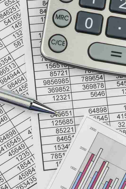 Calculator sitting on pages of statistics with pen and eyeglass