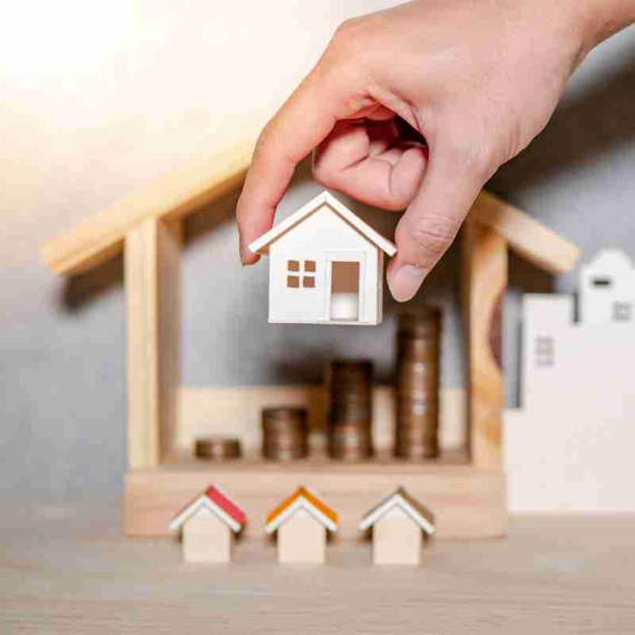 A hand taking small toy house and arranging into a larger toy house symbolizing a real estate investment fund